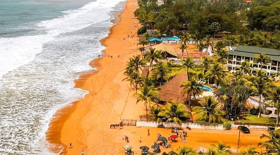 Vue aérienne de la plage de Grand-Bassam avec son sable ocre, ses palmiers et ses complexes hôteliers en bord de mer.