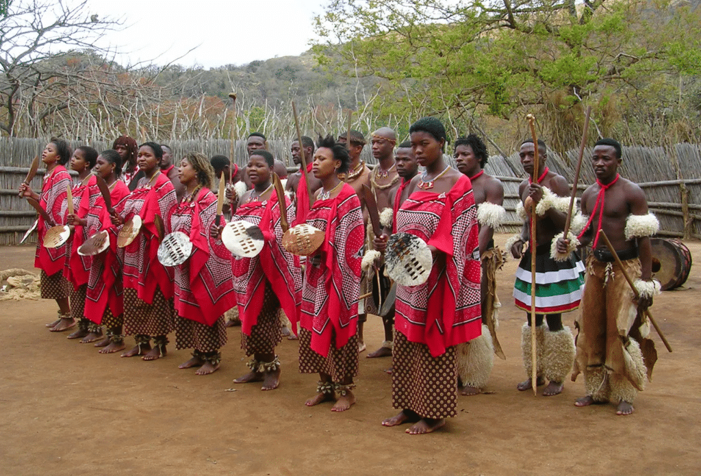 Un groupe d'hommes et de femmes en tenue traditionnelle Swati rouge et noire avec boucliers et lances.