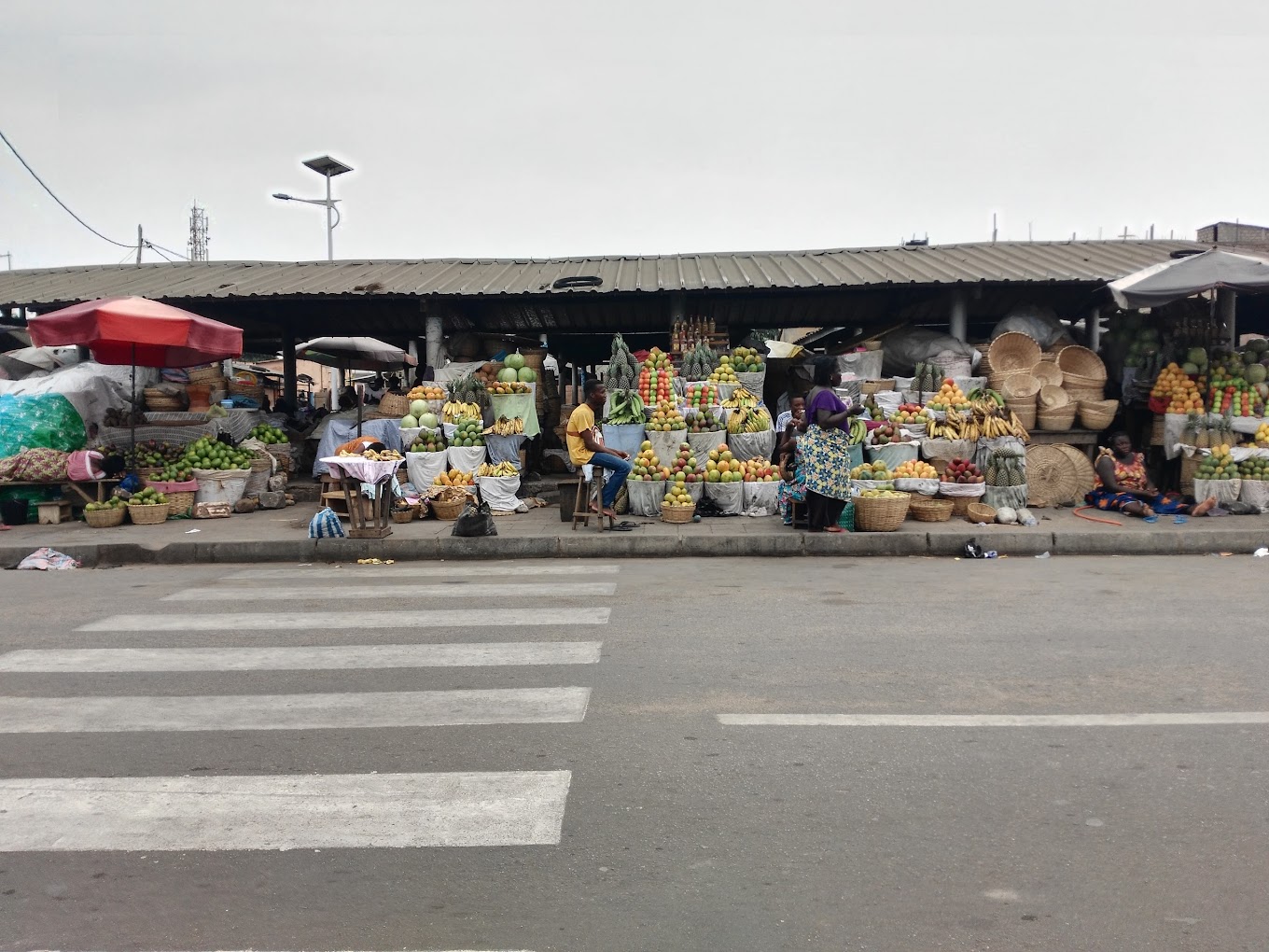 Vue d'un étalage coloré de fruits tropicaux et de paniers au marché de Lomé au Togo, avec des vendeurs assis.