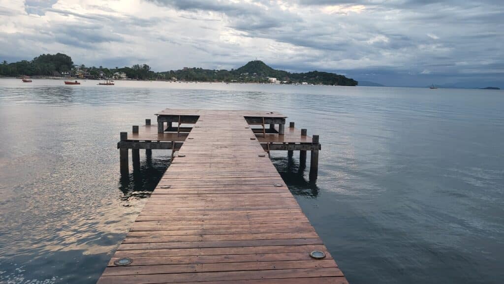 Un long ponton en bois s'avance sur les eaux calmes de la baie d'Ambanoro sous un ciel nuageux à Madagascar.