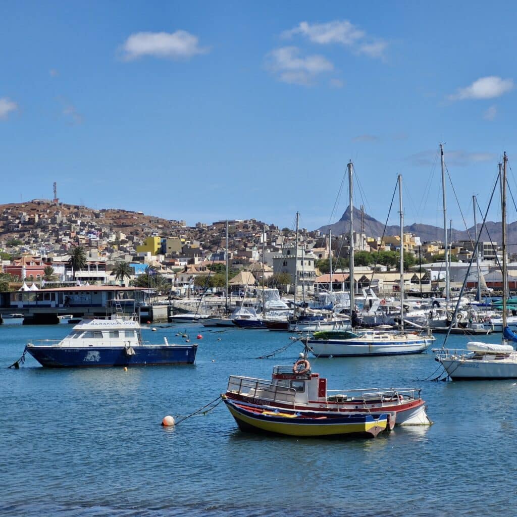 Vue du port de Mindelo à São Vicente avec des bateaux de pêche et des voiliers au mouillage devant la ville ensoleillée.