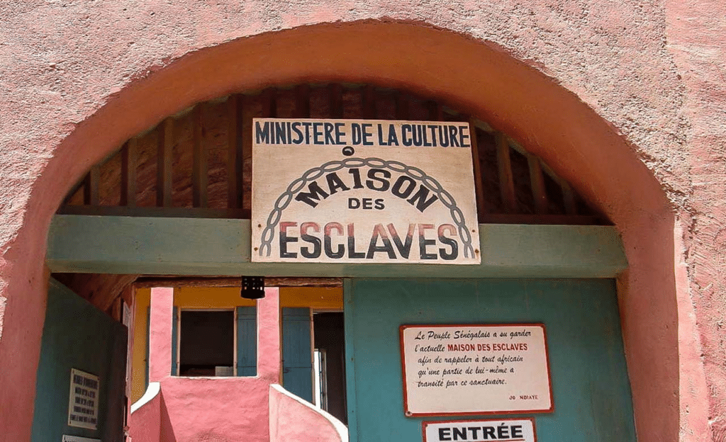 Entrée de la Maison des Esclaves à Gorée, Sénégal, sous une arche rose avec des panneaux d'information en français.