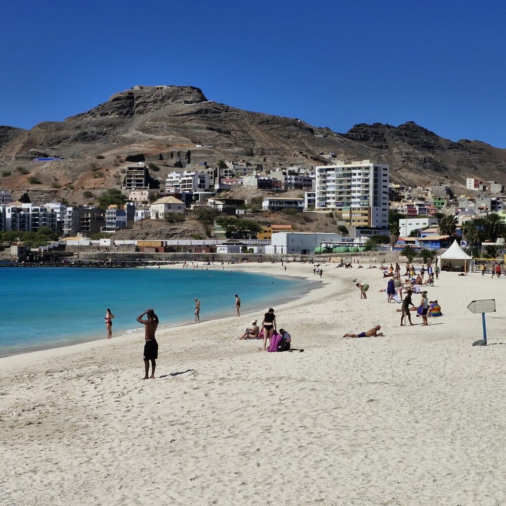 Vue de la plage de Laginha à Mindelo avec son sable blanc, ses baigneurs et les montagnes arides en arrière-plan.
