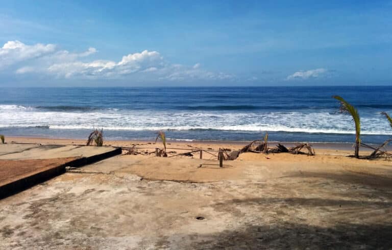 Vue sur l'océan Atlantique depuis une terrasse en béton bordée de palmiers sur la plage de Grand-Bassam.