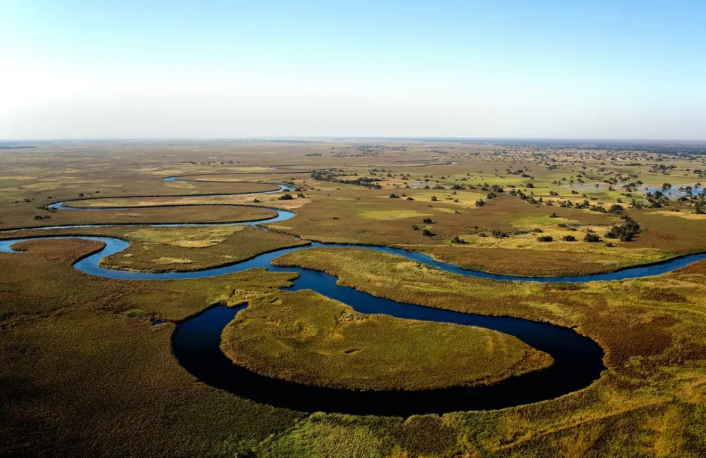 Vue aérienne des méandres d'une rivière bleue serpentant à travers les plaines verdoyantes du delta de l'Okavango.