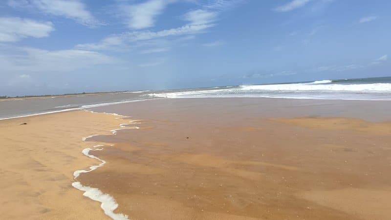 Plage sauvage de sable doré à Grand-Popo au Bénin, bordée par les vagues de l’océan Atlantique sous un ciel bleu parsemé de nuages.