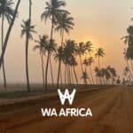 Route de sable bordée de palmiers au bord de l’océan Atlantique, avec un coucher de soleil à l’horizon. Logo blanc "WA AFRICA" au centre de l’image.