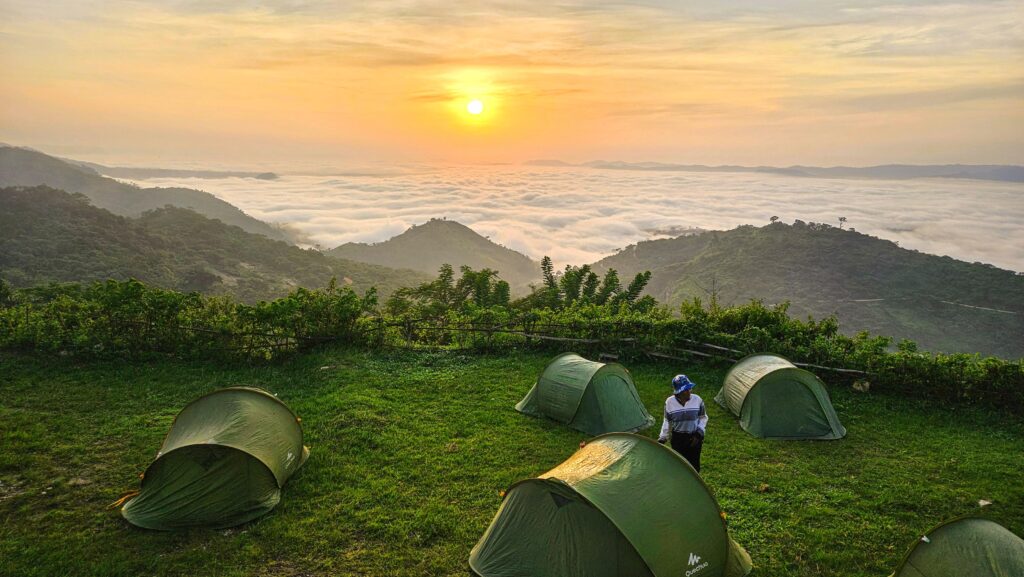 Camping au lever du soleil sur les montagnes des Plateaux au Togo, avec des tentes vertes face à une mer de nuages.