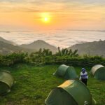 Camping au lever du soleil sur les montagnes des Plateaux au Togo, avec des tentes vertes face à une mer de nuages.