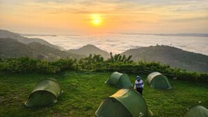 Camping au lever du soleil sur les montagnes des Plateaux au Togo, avec des tentes vertes face à une mer de nuages.