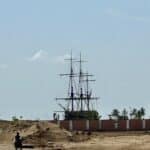 Réplique du navire historique à Ouidah au Bénin, vue depuis une zone sablonneuse avec un motocycliste au premier plan