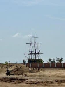 Réplique du navire historique à Ouidah au Bénin, vue depuis une zone sablonneuse avec un motocycliste au premier plan