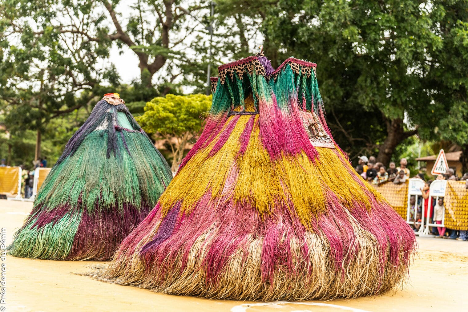 Deux masques traditionnels Zangbéto en fibres de raphia colorées (jaune, rose, vert) lors du festival des masques au Bénin.