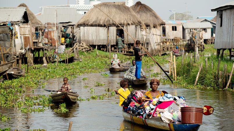 Scène de vie quotidienne à Ganvié, village lacustre sur pilotis au Bénin avec des pirogues sur l'eau.