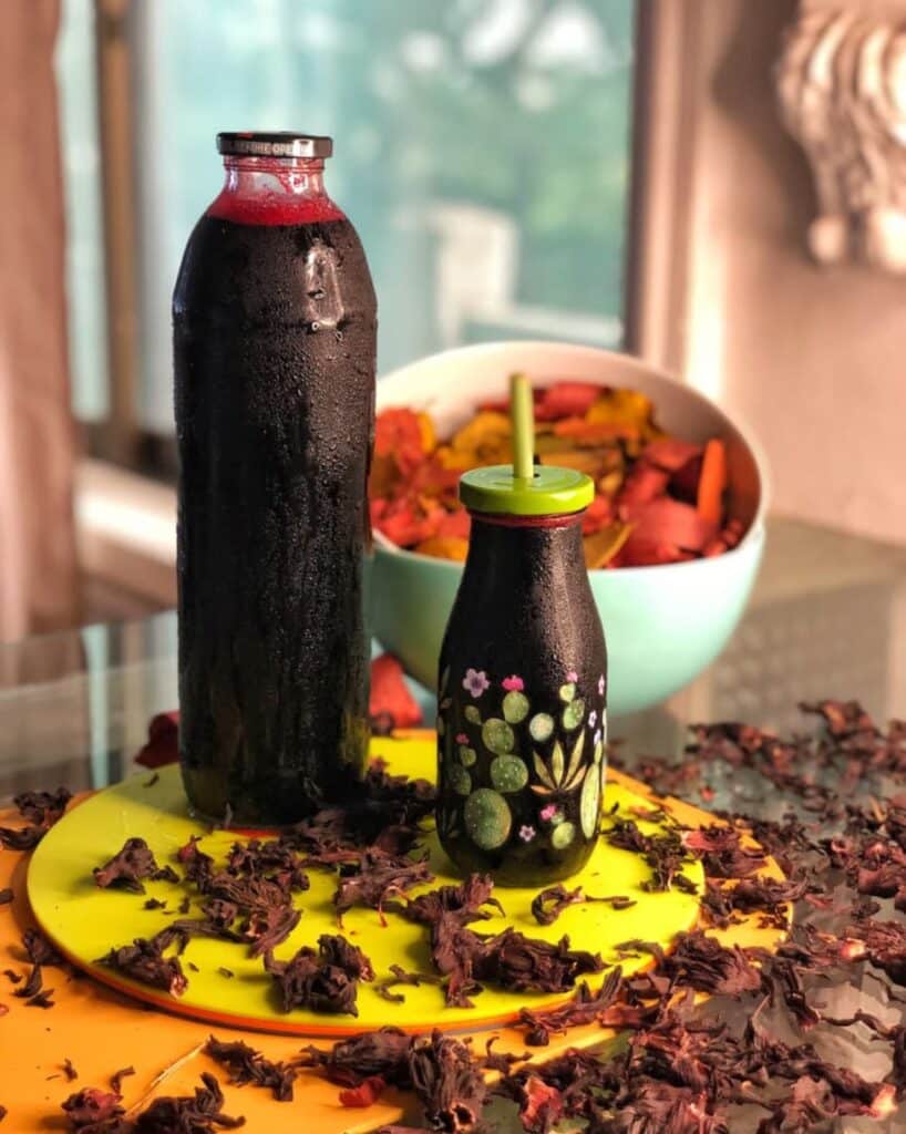 Bouteilles de jus de bissap frais (hibiscus) avec fleurs séchées sur une table, boisson traditionnelle du Bénin.