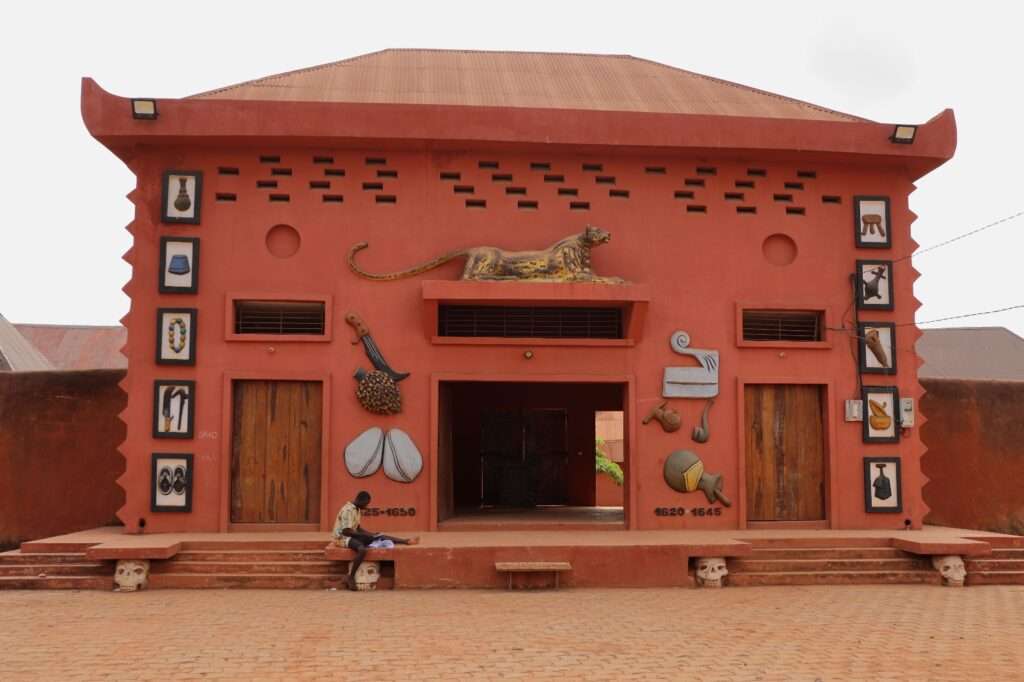 Façade rouge ocre du musée des Palais Royaux d'Abomey avec bas-reliefs représentant un lion et des symboles royaux du Dahomey.
