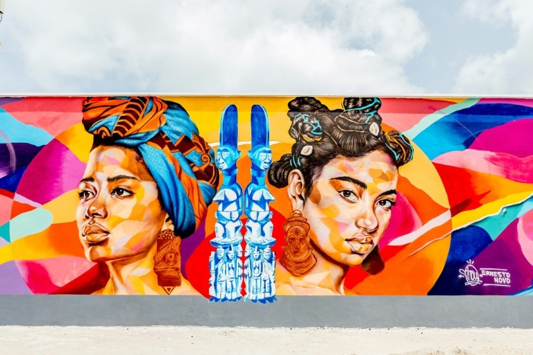 Fresque murale représentant deux visages de femmes africaines et des statues traditionnelles à Cotonou.