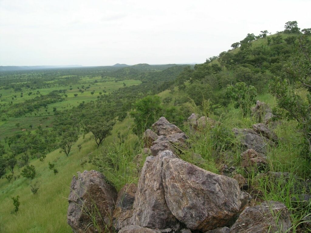 Vue panoramique des paysages montagneux et vallonnés de la chaîne de l'Atacora avec des rochers au premier plan et une vaste savane verdoyante au Bénin.