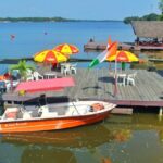 Un bateau à moteur orange amarré à un ponton en bois avec des parasols colorés sur la lagune à l'île Boulay.
