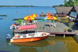 Un bateau à moteur orange amarré à un ponton en bois avec des parasols colorés sur la lagune à l'île Boulay.