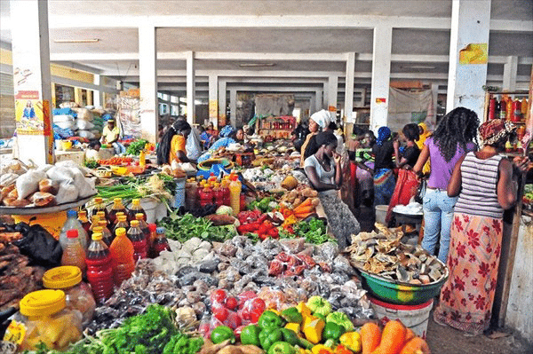 Des étals colorés de légumes, fruits et huiles dans un grand marché couvert animé à Ziguinchor au Sénégal.