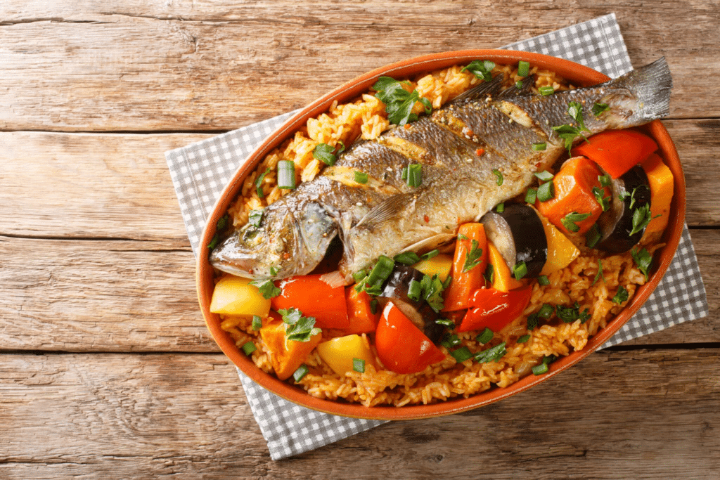 Un plat de Thiéboudienne composé de riz rouge, d'un poisson entier grillé et de légumes variés.