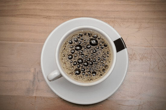 Une tasse de café Touba noir avec une mousse onctueuse vue de dessus sur une table en bois.