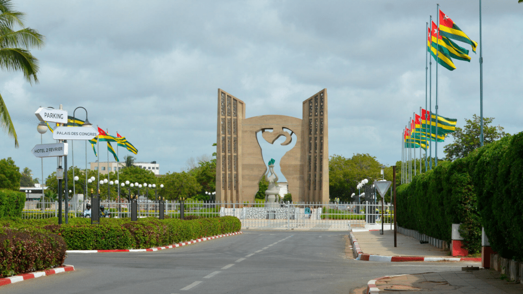 Le Mémorial de l'Indépendance à Lomé, monument en béton sculpté entouré de drapeaux togolais sous un ciel nuageux.