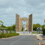 Le Mémorial de l'Indépendance à Lomé, monument en béton sculpté entouré de drapeaux togolais sous un ciel nuageux.