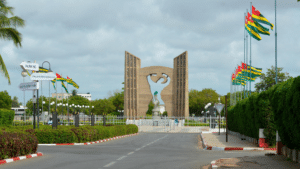 Le Mémorial de l'Indépendance à Lomé, monument en béton sculpté entouré de drapeaux togolais sous un ciel nuageux.