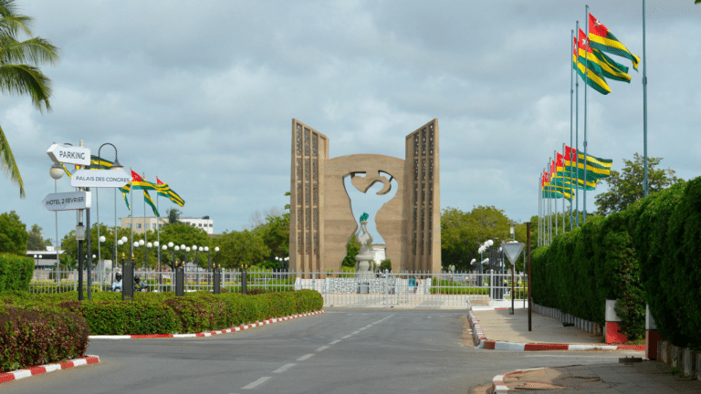 Le Mémorial de l'Indépendance à Lomé, monument en béton sculpté entouré de drapeaux togolais sous un ciel nuageux.