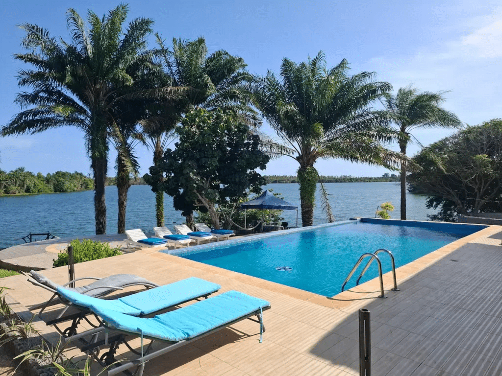 Une piscine à débordement avec des transats bleus face à la lagune bordée de palmiers à l'île Boulay.