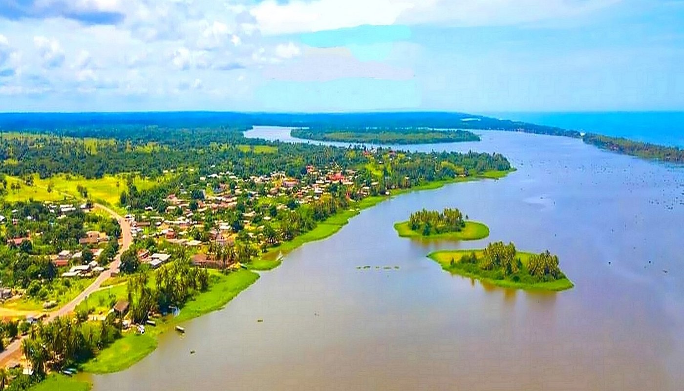 Vue aérienne de Grand-Lahou montrant un vaste plan d’eau entouré de végétation tropicale, de petits îlots verdoyants et d’habitations le long de la rive.
