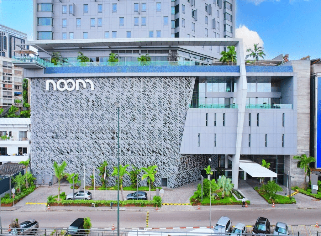 Façade moderne grise avec motif perforé et logo Noom, surmontée d'une piscine à débordement à Abidjan.