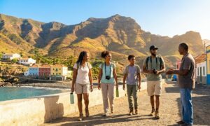 Une famille de voyageurs de la diaspora africaine et caribéenne échangeant avec un guide local sur un front de mer ensoleillé, avec des montagnes et des maisons colorées en arrière-plan.