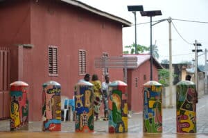 Potelets décorés de fresques colorées sur la Place Chacha à Ouidah devant un bâtiment en terre battue.