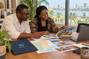 Deux personnes afro-descendantes souriantes, assises à une table en bois, parcourent une brochure de voyage pour planifier un séjour en Afrique.